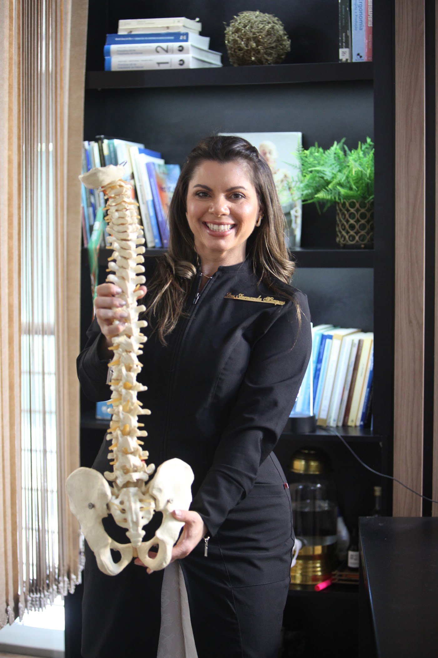 Dra. Fernanda Marques, fisioterapeuta e fundadora do Instituto Valens, segurando um modelo da coluna vertebral