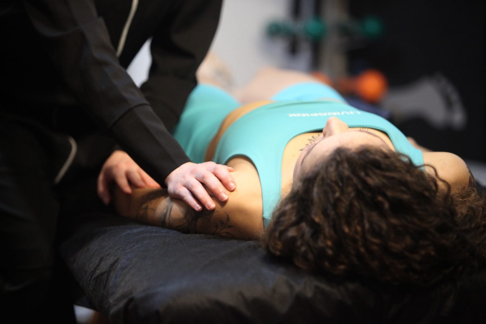 Terapia manual na coluna: mãos do profissional posicionando o ombro de uma paciente deitada na maca